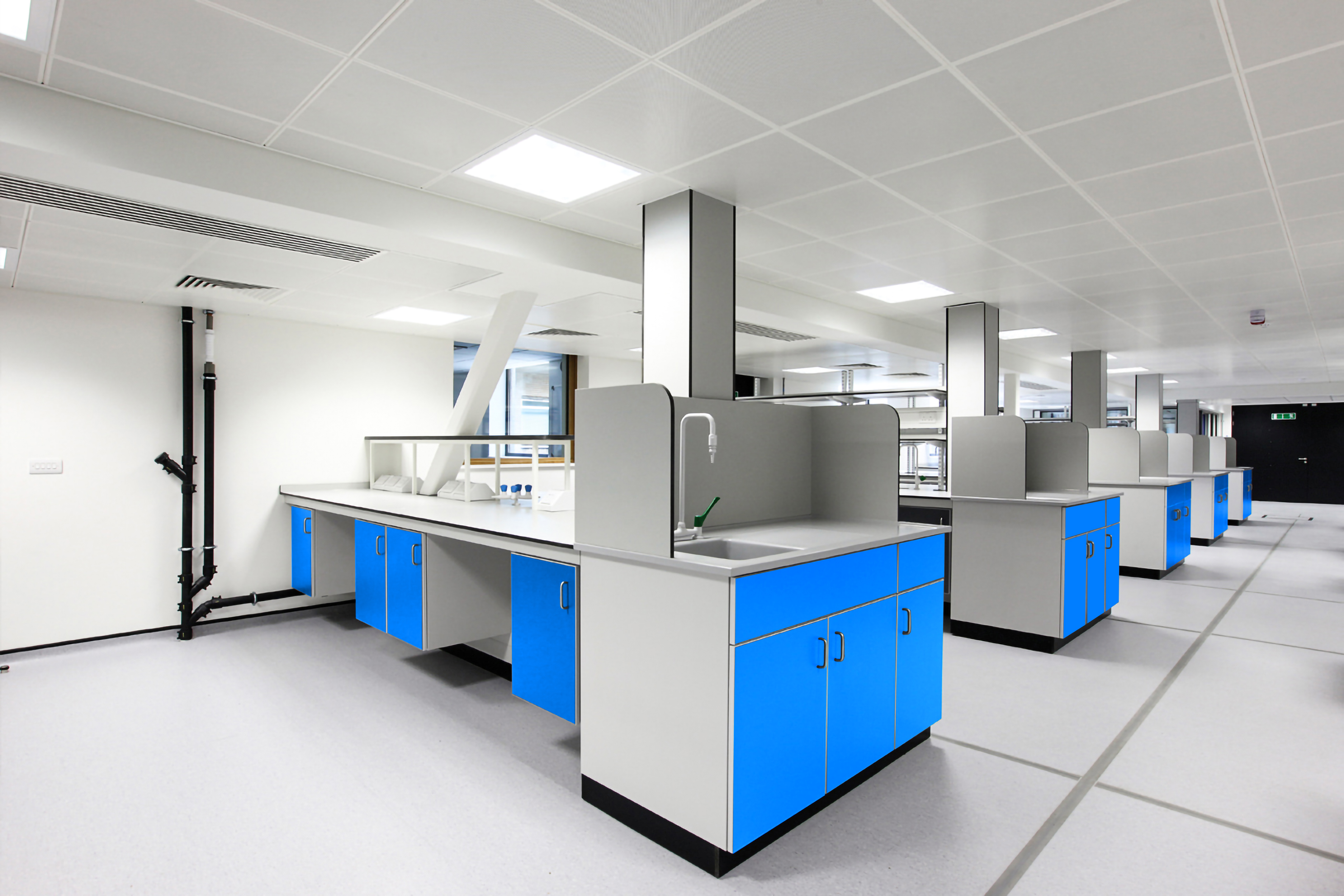 Modern laboratory featuring modular island workbenches with blue cabinets, grey chemical-resistant worktops, and integrated sink units.
